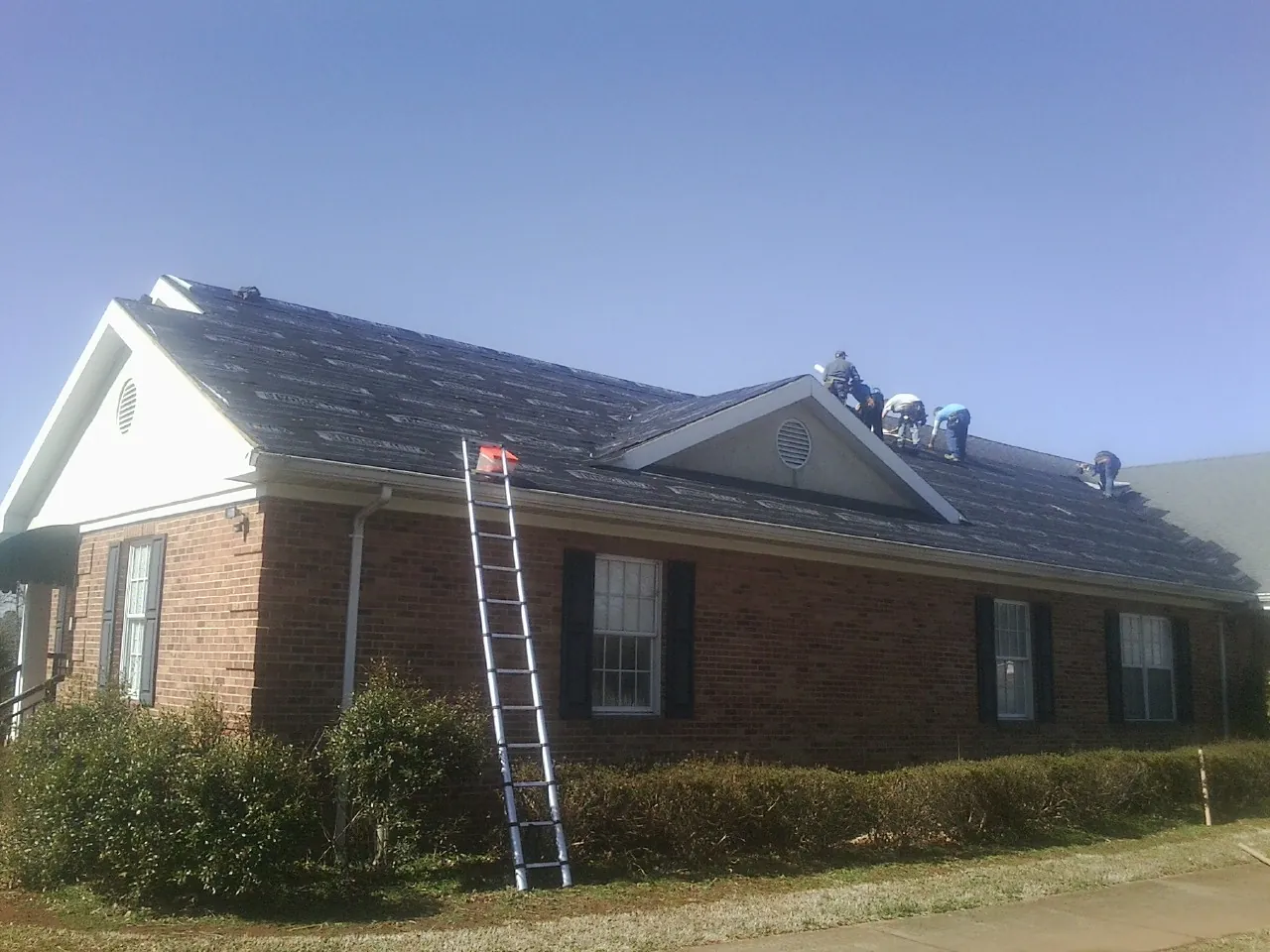 Crew tearing shingles off a brick ranch roof with a ladder set — Metal Roof Repair work by our crew in Ardara