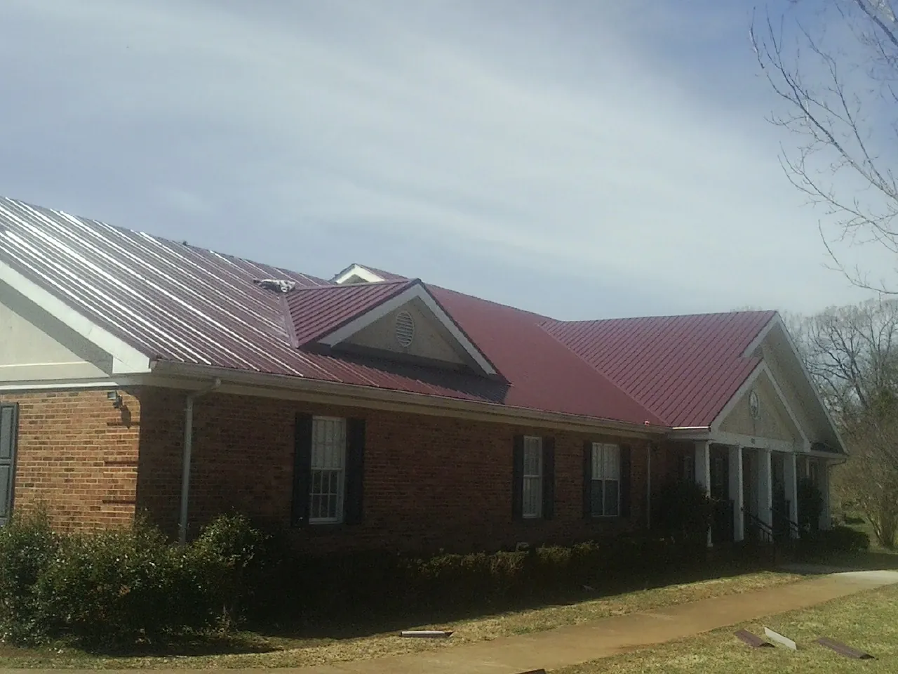 Red metal roof with gabled entries on a long brick building, from a Hail Damage Roof Repair job in Ardara
