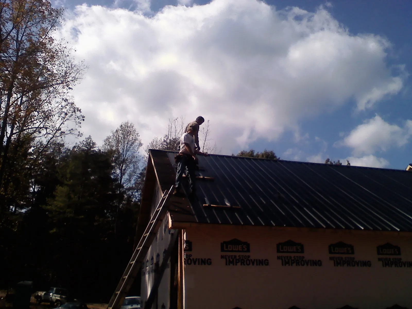 Roofer fastening dark metal panels high against a cloudy sky, from a Roof Inspection job in Ardara