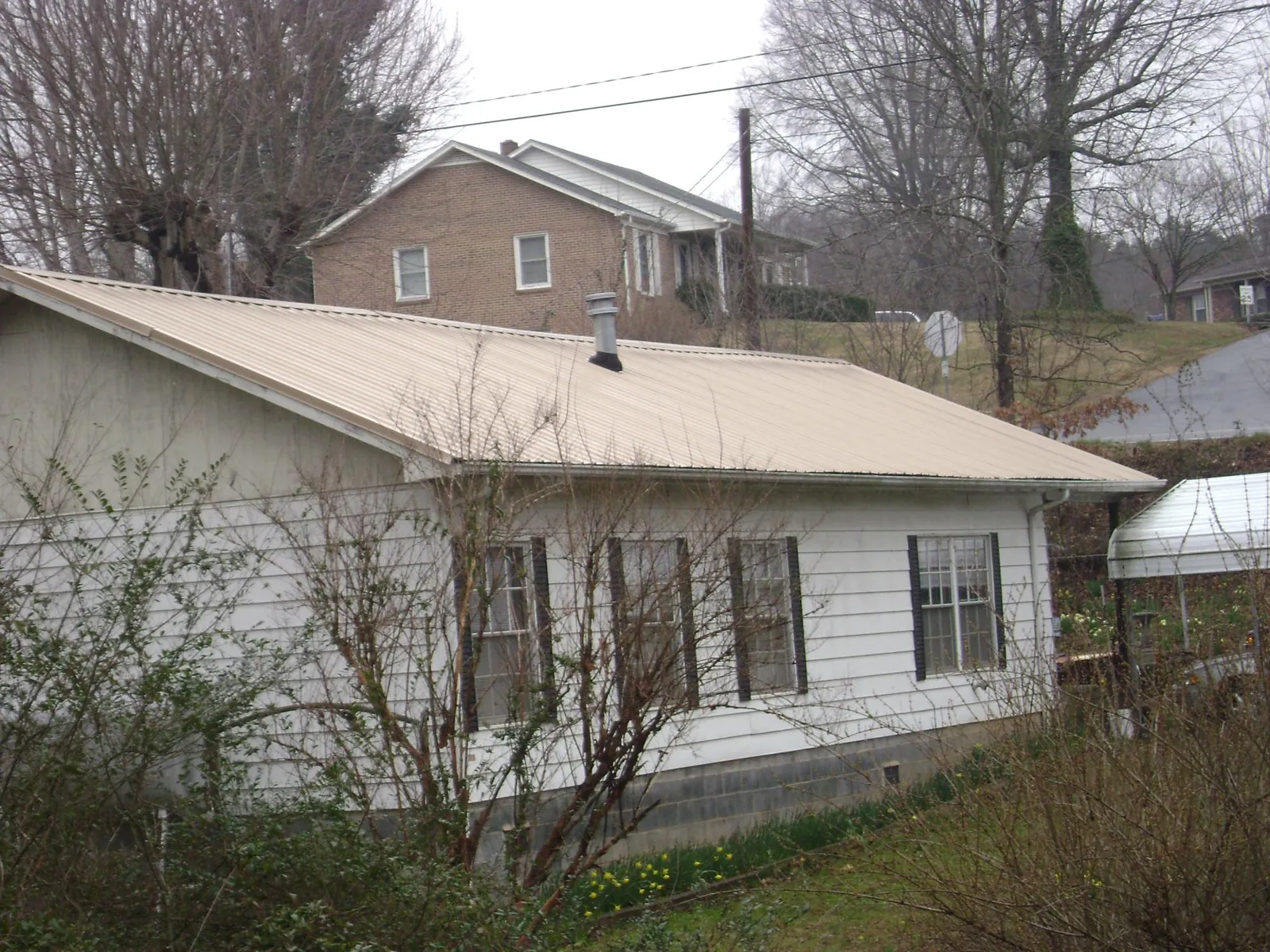 Tan metal roof on a white sided house set into a hillside — Commercial Roofing by Roofing Brothers in Ardara